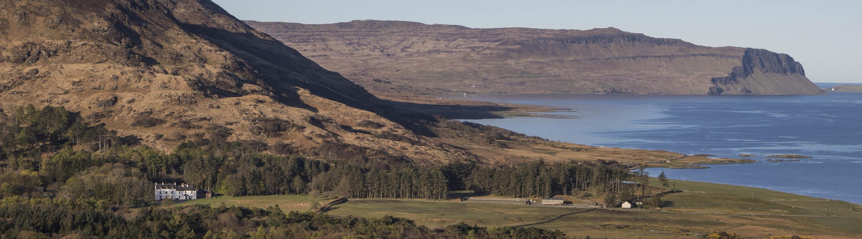 Benmore Estate  view with Knock House, view from high looking down onto landscape with hills behind woodland, running down to the sea. Headland in the distance